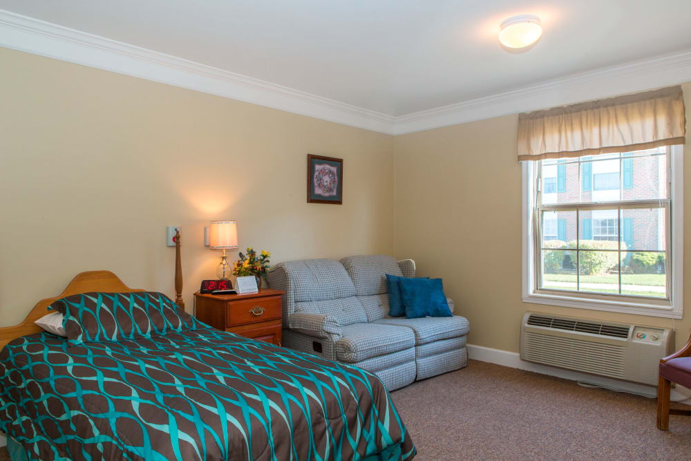 Upscale bedroom in senior living facility with sofa seating and window light at Carriage Court of Washington Court House in Washington Court House, Ohio