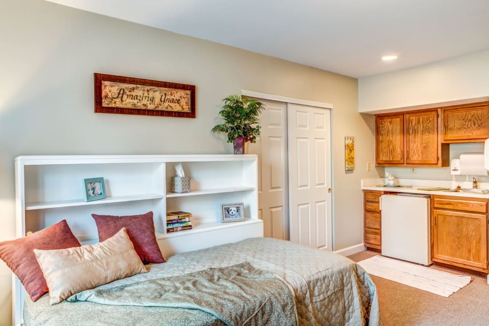 Cozy bed with wood accented kitchen in apartment at Carriage Court of Lancaster in Lancaster, Ohio