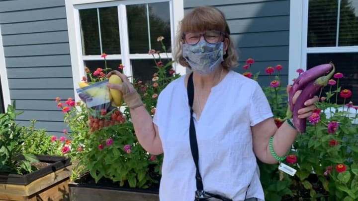 Woman-outside-with-mask-in-summer-holding-vegetables-in-garden