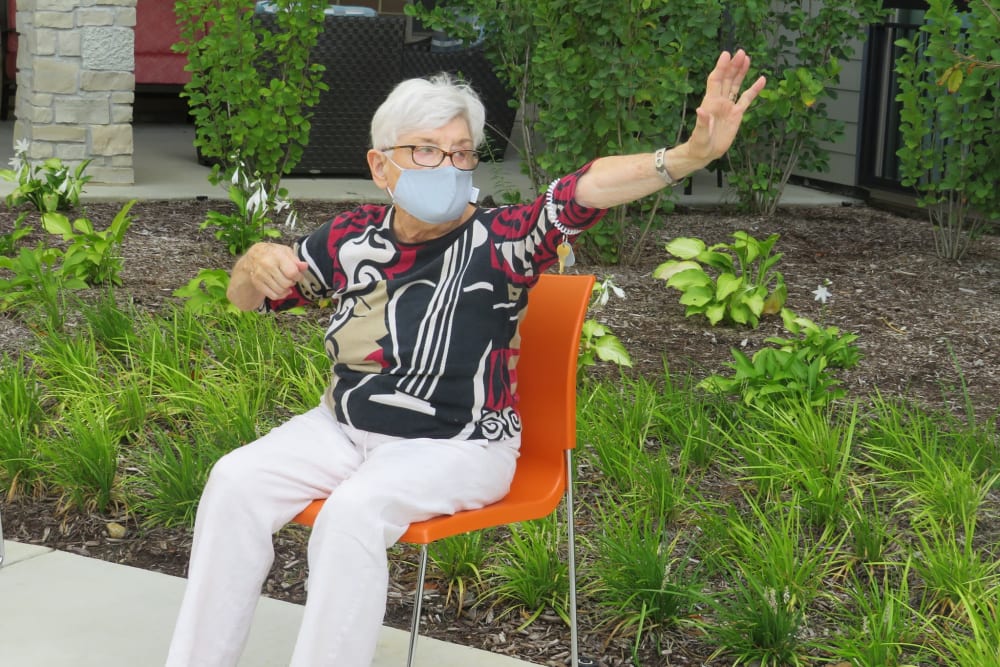 Resident sitting on an orange chair waving to somebody at Aspired Living of La Grange in La Grange, Illinois