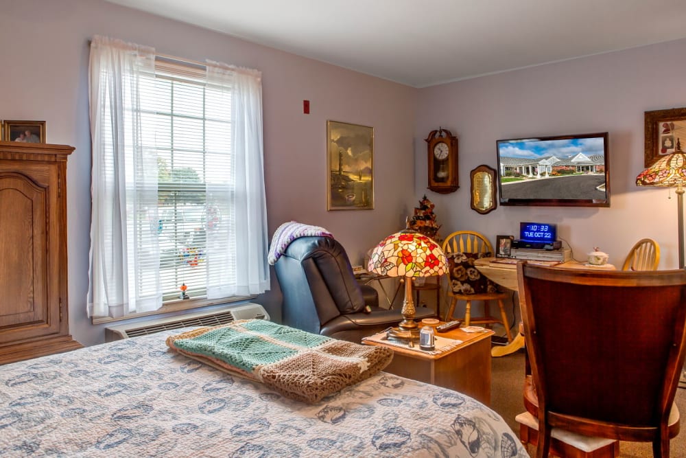 Cheerful apartment in upscale senior living facility complete with bed, seating, and television set at Carriage Court of Grove City in Grove City, Ohio
