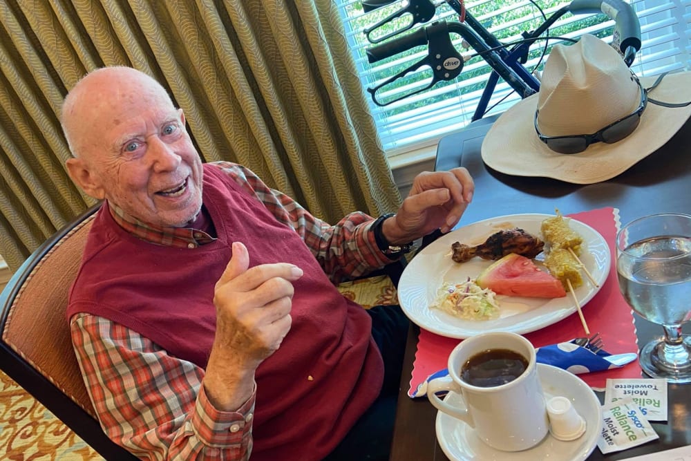 Male resident in red shirt smiling and giving thumbs up in dining room with delicious food at Azpira at Windermere | Pathway to Living